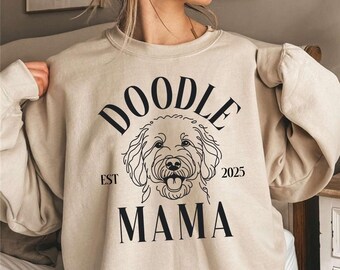 Puede incluir: Una sudadera beige con un gráfico de perro doodle negro y el texto "Doodle Mama Est 2025".