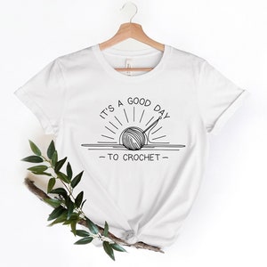 May include: White t-shirt with a black line drawing of a yarn ball and crochet hook in the shape of a sun with the text "It's a good day to crochet."