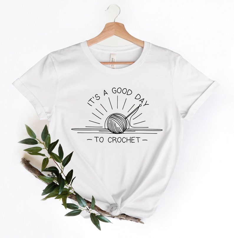 May include: White t-shirt with a black line drawing of a yarn ball and crochet hook in the shape of a sun with the text "It's a good day to crochet."
