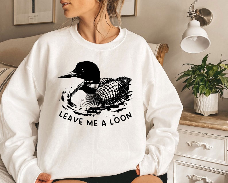 May include: White sweatshirt with a black and white illustration of a loon swimming. The text "Leave me a loon" is printed below the loon.