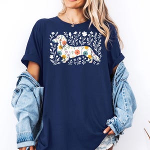 May include: Navy blue t-shirt featuring a floral dachshund design. The dog is filled with colorful flowers and surrounded by white floral accents. The shirt has short sleeves and a relaxed fit.