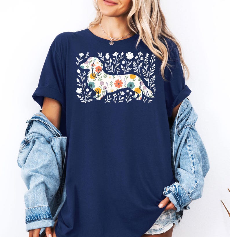 May include: Navy blue t-shirt featuring a floral dachshund design. The dog is filled with colorful flowers and surrounded by white floral accents. The shirt has short sleeves and a relaxed fit.
