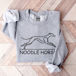 May include: Gray sweatshirt with a black line drawing of a greyhound dog running and the text "NOODLE HORSE" underneath.