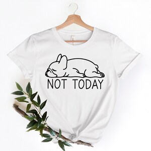 May include: White t-shirt featuring a black line drawing of a sleeping French bulldog and the text "NOT TODAY".