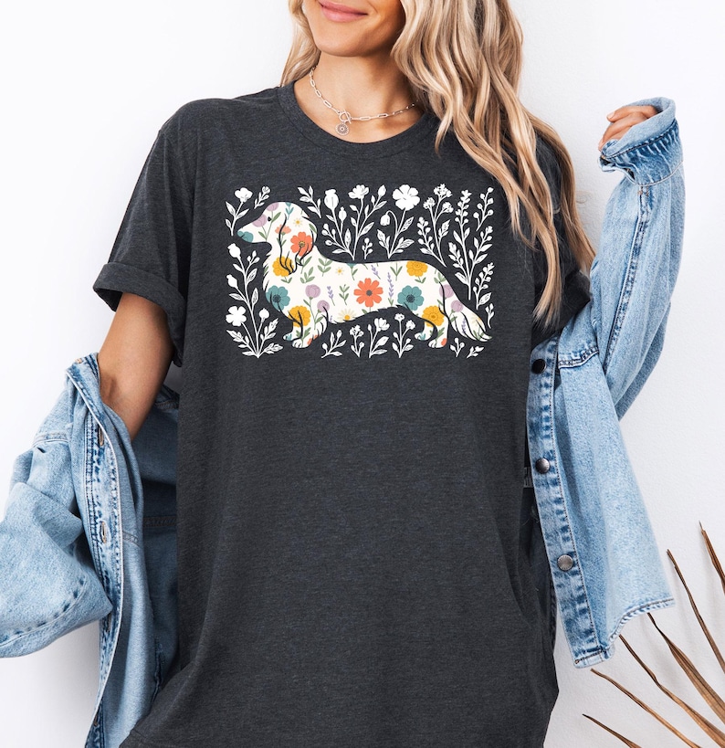 May include: Dark gray t-shirt featuring a floral dachshund design. The dog is filled with colorful flowers and surrounded by white floral elements. The shirt has short sleeves and a relaxed fit.