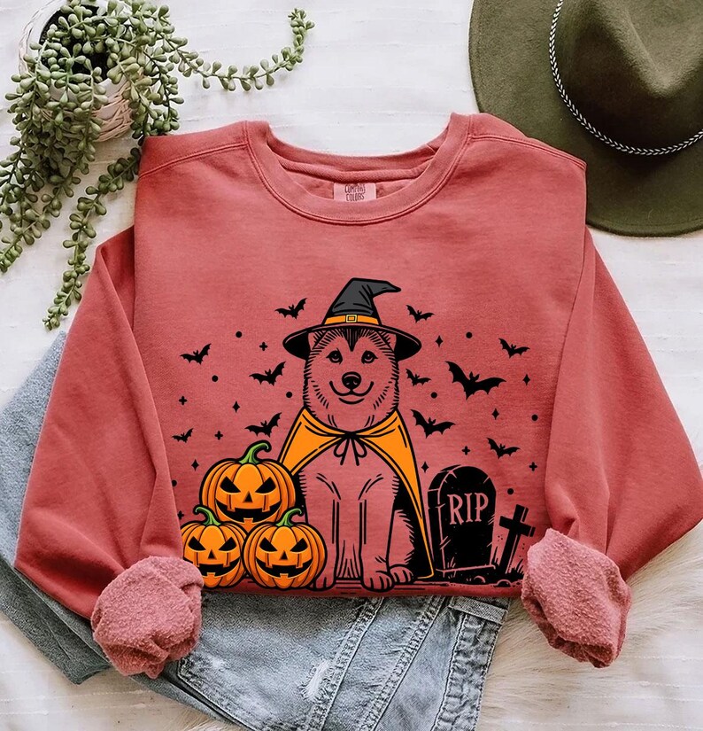 May include: A red sweatshirt with a Halloween-themed design featuring a dog wearing a witch hat and cape, pumpkins, and a tombstone with the inscription "RIP".