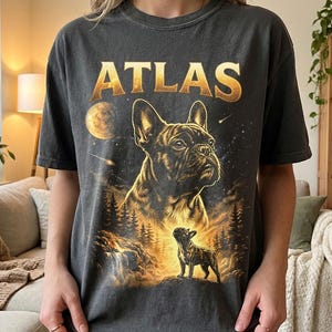 May include: Dark gray t-shirt featuring a golden illustration of a French Bulldog with the word "ATLAS" in gold lettering above. The design includes a night sky, moon, and a smaller dog silhouette.
