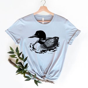 May include: A light blue t-shirt with a black and white illustration of a loon swimming in water.
