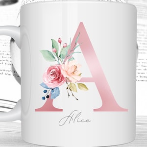 Peut inclure: Mug en céramique blanche avec un motif floral rose comprenant la lettre "A" et le nom "Alice" en écriture cursive.
