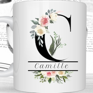 Peut inclure: Mug en céramique blanche avec une lettre C noire décorée de fleurs et de feuillage aquarelle. Le nom "Camille" est écrit sous la lettre.