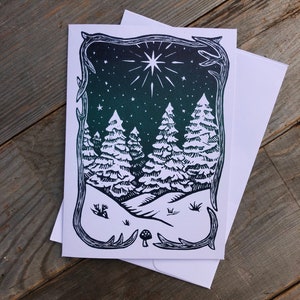 Puede incluir: Una ilustraci&oacute;n en blanco y negro de una escena de bosque nevado con una gran estrella en el cielo nocturno. La ilustraci&oacute;n est&aacute; enmarcada con un borde decorativo.