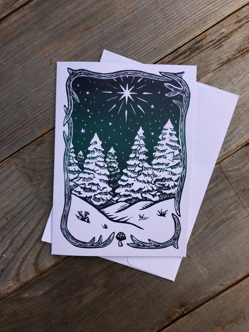 Puede incluir: Una ilustraci&oacute;n en blanco y negro de una escena de bosque nevado con una gran estrella en el cielo nocturno. La ilustraci&oacute;n est&aacute; enmarcada con un borde decorativo.