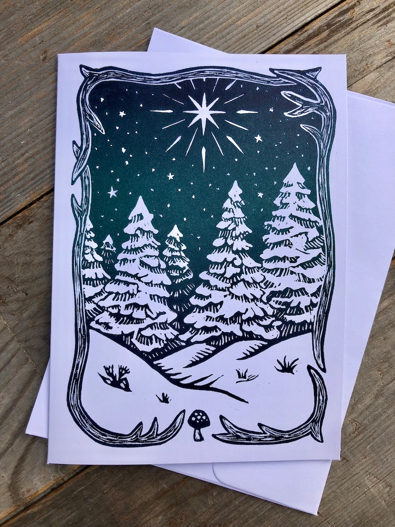 Puede incluir: Una impresi&oacute;n en lin&oacute;leo en blanco y negro de una escena de bosque nevado con una gran estrella en el cielo nocturno. La impresi&oacute;n est&aacute; enmarcada con un borde decorativo.