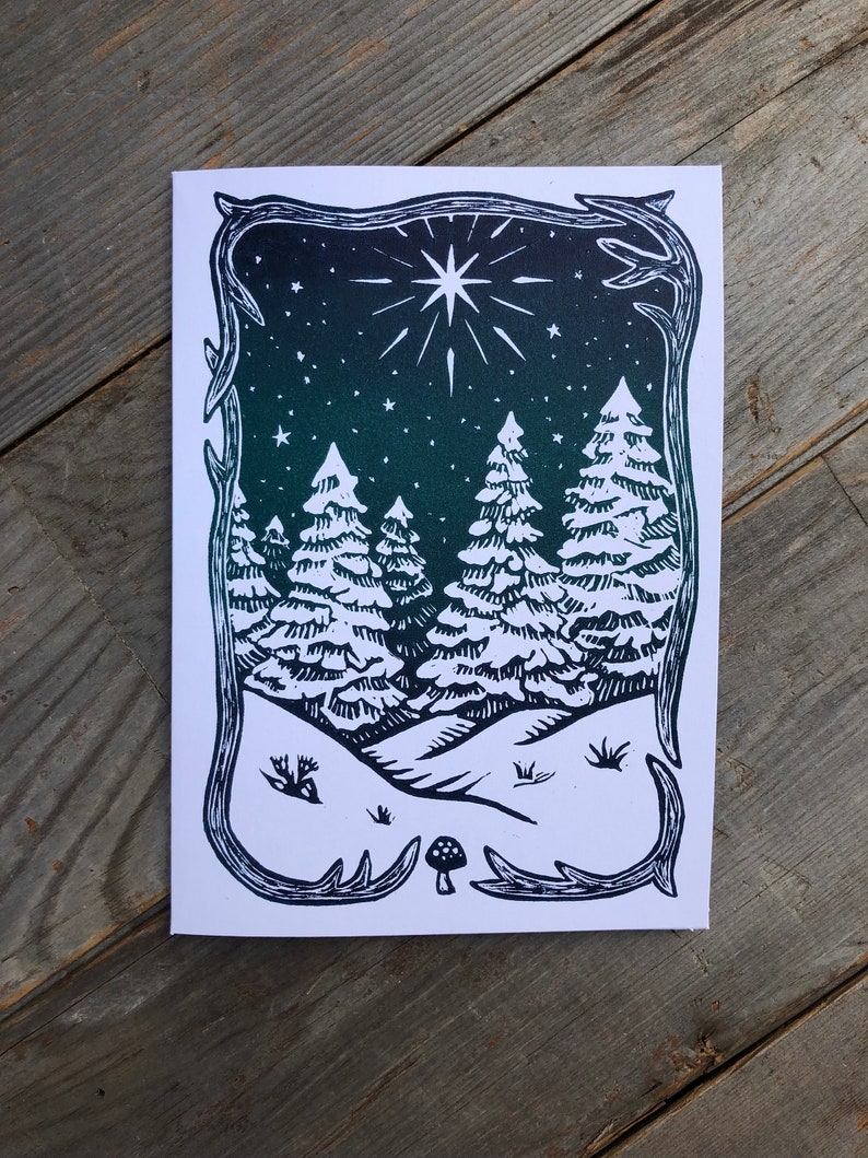 Puede incluir: Una impresi&oacute;n en lin&oacute;leo en blanco y negro de una escena de bosque de invierno con una gran estrella en el cielo nocturno. La impresi&oacute;n est&aacute; enmarcada con un borde decorativo.