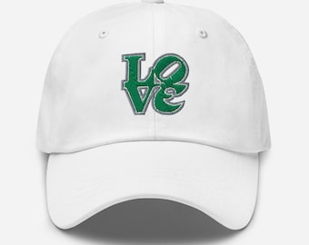 May include: White baseball cap with the word "Love" embroidered in green with a gray outline. The cap has a curved brim and an adjustable strap at the back.