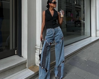 Calça jeans de perna larga com efeito desgastado e patchwork listrado, estilo streetwear arrojado dos anos 2000.