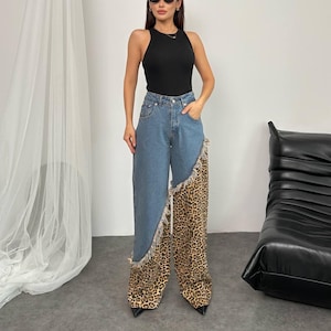 Puede incluir: Un top negro combinado con vaqueros de mezclilla azules con un panel único con estampado de leopardo en una pierna. Los vaqueros tienen un borde deshilachado. El atuendo se completa con gafas de sol negras.