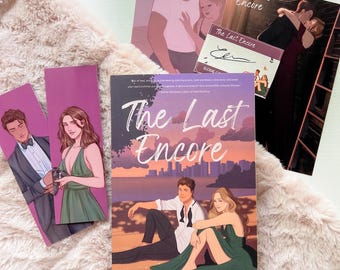 May include: A paperback novel titled "The Last Encore" by Elodie Colliard. The cover features a couple sitting on a beach at sunset. The book is surrounded by other items, including a bookmark and a signed bookplate.