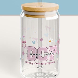 Pode incluir: Uma garrafa de água de vidro transparente com um design rosa e branco. A garrafa tem uma tampa de bambu e um canudo. O design inclui as letras "DCP" com o texto "magic maker" e "Disney College Program".