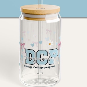 Pode incluir: Um copo de vidro transparente com tampa de bambu e canudo transparente. O copo apresenta um design com o texto "DCP magic maker!" em azul, juntamente com laços, corações e flores. As palavras "Disney College program" também estão impressas.