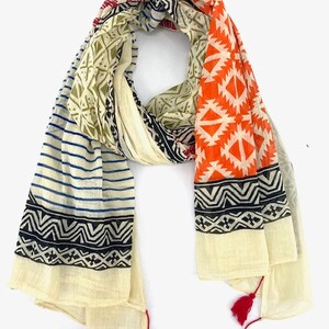 May include: A cream-colored cotton scarf with a geometric pattern in orange, blue, black, and green. The scarf has red tassels on each end.