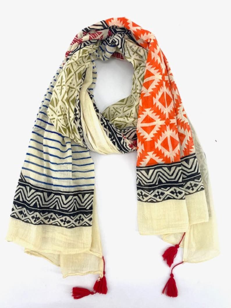 May include: A cream-colored cotton scarf with a geometric pattern in orange, blue, black, and green. The scarf has red tassels on each end.