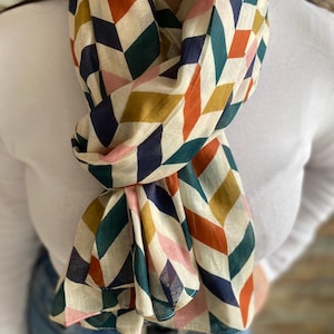 May include: A white scarf with a geometric pattern in shades of red, orange, yellow, green, blue, and pink. The pattern is made up of diamonds and squares.