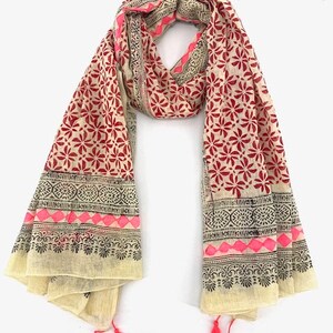 May include: A cream-colored cotton scarf with a red and black floral print and pink accents. The scarf has a black and white border with a geometric pattern and tassels on the ends.