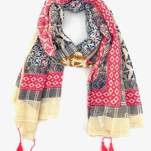 May include: A cream-colored cotton scarf with a pink, blue, and brown geometric pattern. The scarf has tassels on each end.