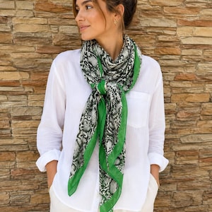 Peut inclure: Écharpe à imprimé serpent noir et blanc avec une bordure verte. Le motif de l'écharpe est un mélange de noir, de blanc et de gris, créant un contraste saisissant avec la bordure verte. Un accessoire de mode, porté sur une chemise blanche.