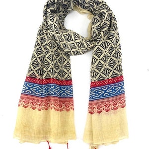 May include: A cream-colored scarf with a black and white geometric pattern. The scarf has red, blue, and white trim and red tassels.