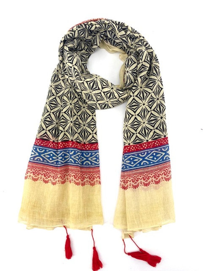 May include: A cream-colored scarf with a black and white geometric pattern. The scarf has red, blue, and white trim and red tassels.
