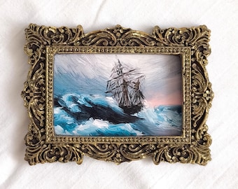 Kleine schilderijprint van een stormachtige zee en een oud schip, ingelijst met een gouden nautische kunstprint.