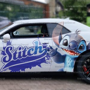 May include: White car side panel with a large blue and white "Stitch" graphic. The design includes the word "Stitch" in a stylized font, and an illustration of the character. The car has black wheels and red brake calipers.