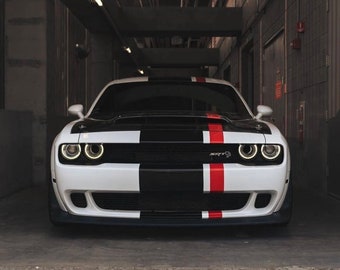 May include: A white sports car with black and red racing stripes. The front of the car features a black grille and the text "SRT". The car is parked in a garage.