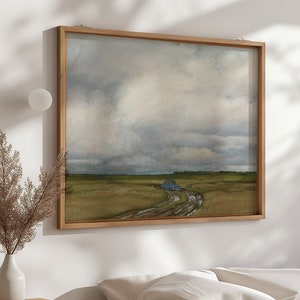 Puede incluir: Una pintura enmarcada de un coche azul conduciendo por un camino de tierra a través de un campo. El cielo está nublado y gris. La pintura está en un marco de madera.