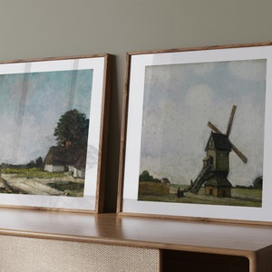 Könnte beinhalten: Zwei gerahmte Landschaftsbilder mit einem rustikalen Holzrahmen. Das Bild links zeigt eine ländliche Szene mit einem Bauernhaus und einem Baum. Das Bild rechts zeigt eine Windmühle auf einem Feld.