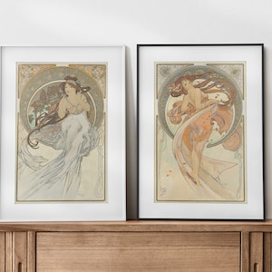 Peut inclure: Deux impressions d'art encadrées représentant des illustrations de style Art nouveau de femmes en robes flottantes. Les impressions sont dans des cadres blancs et noirs et sont exposées sur une étagère en bois.