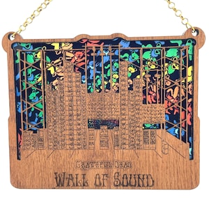May include: A wooden wall art ornament featuring a detailed illustration of the Grateful Dead's "Wall of Sound" stage setup. The background is a colorful pattern of dancing bears. The text "GRATEFUL DEAD WALL OF SOUND" is printed below the illustration.