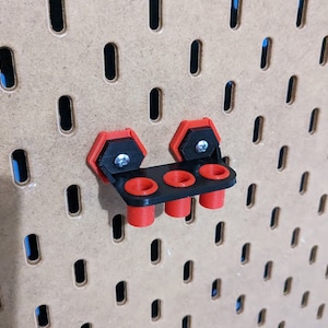 May include: A black and red pegboard tool holder with three slots for holding tools. The holder is mounted on a pegboard.