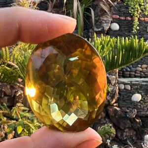 May include: A large, faceted, golden yellow gemstone with a slight green hue. The gemstone is cut into a round shape and has a smooth, polished surface.