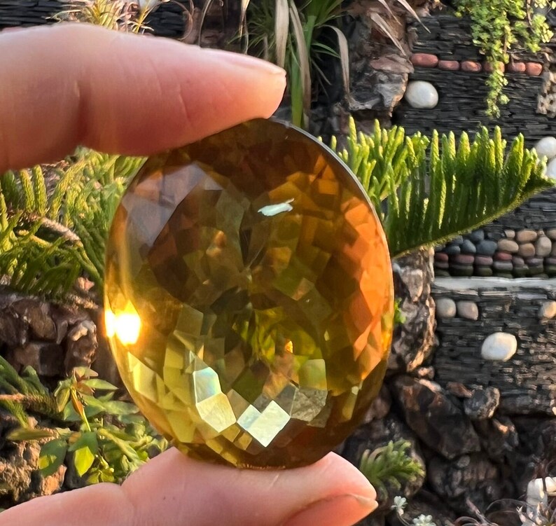 May include: A large, faceted, golden yellow gemstone with a slight green hue. The gemstone is cut into a round shape and has a smooth, polished surface.