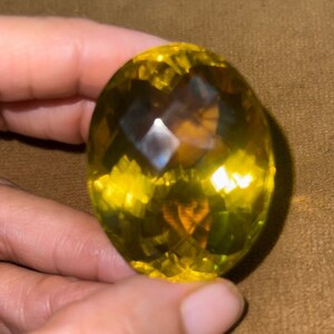 May include: A large, oval-shaped, yellow gemstone with a faceted cut. The gemstone has a slightly darker yellow center and a lighter yellow outer edge.