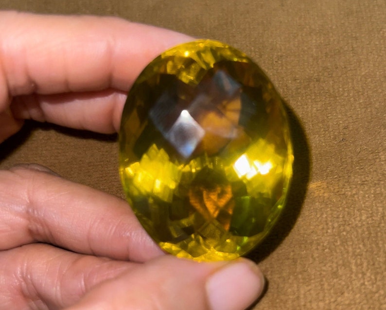 May include: A large, oval-shaped, yellow gemstone with a faceted cut. The gemstone has a slightly darker yellow center and a lighter yellow outer edge.