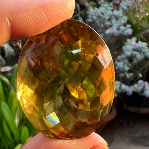 May include: A large, faceted, oval-shaped gemstone with a golden yellow color and green and iridescent hues.
