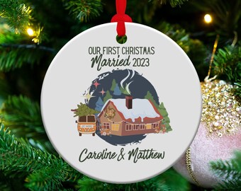 May include: A white round Christmas bauble with a blue and white illustration of a cabin in the snow with a vintage van in front of it. The text "Our First Christmas Married 2023" is at the top and "Caroline & Matthew" is at the bottom.