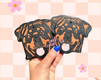 May include: Two black and brown Rottweiler dog head shaped air fresheners with the text "SWEET CLOUDS + CO" on one of the air fresheners.