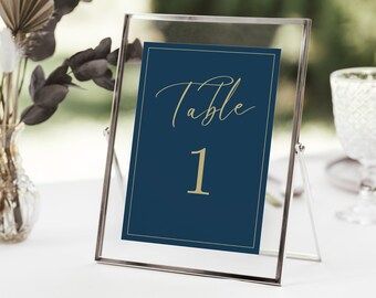 May include: A navy blue table number card with gold lettering that reads "Table 1" in a clear acrylic frame.