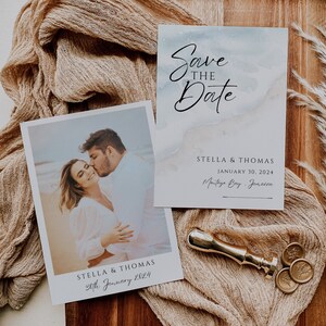 May include: Save the Date card with a watercolor background in shades of blue and beige. The card features the text "Save the Date" in black calligraphy and the names "Stella & Thomas" with the date "January 30, 2024" and location "Montego Bay, Jamaica". A photo of a couple kissing on a beach is included on a separate card with the text "Stella & Thomas" and "30th January 2024".