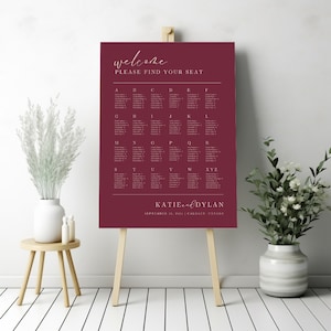 Könnte beinhalten: Eine burgunderfarbene Hochzeitsplatzkarte mit weißem Text. Die Karte trägt den Titel "Willkommen, bitte finden Sie Ihren Platz". Die Karte listet die Namen der Gäste alphabetisch nach Tischbuchstaben auf. Am unteren Rand der Karte steht "Katie und Dylan, 13. September 2024, Calgary, Kanada."